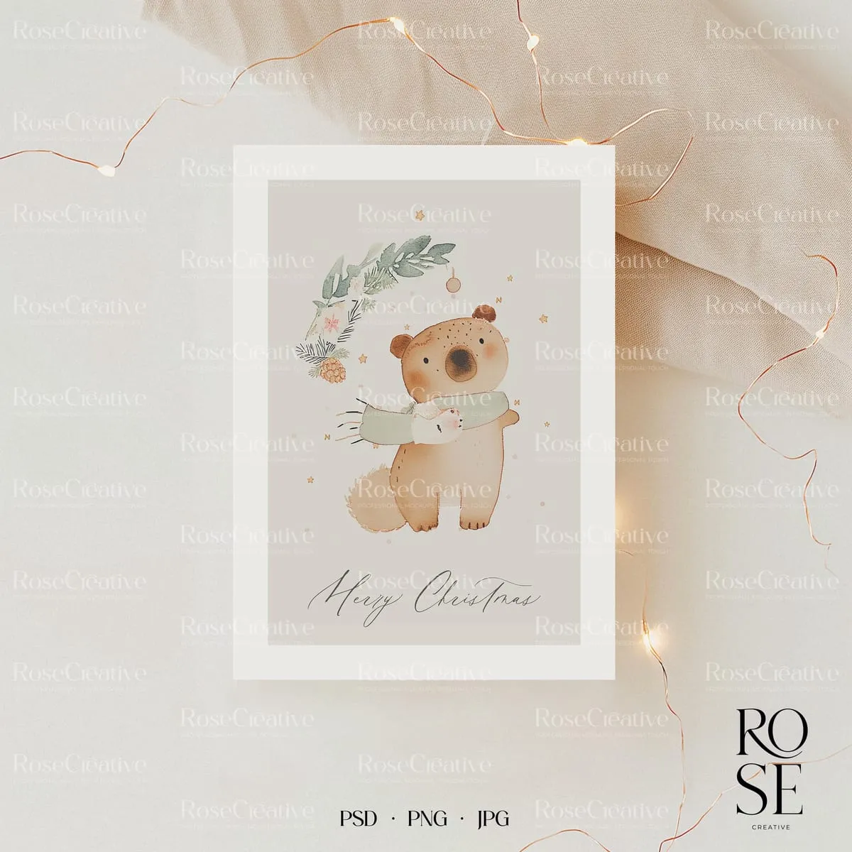 Mockup Rose Creative Atelier : carte de Noël illustrée d’un ourson, sur un drapé clair et une guirlande lumineuse.